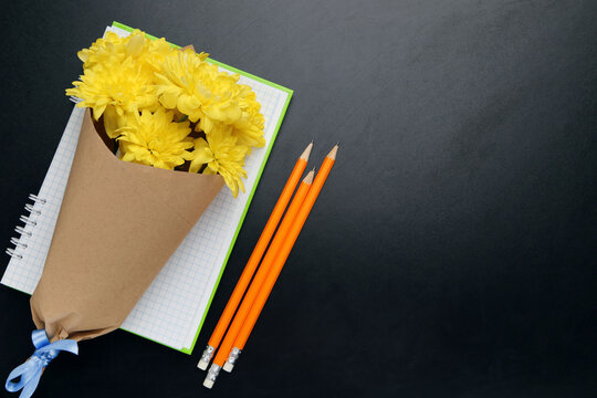 Bouquet of yellow chrysanthemums, notepad and orange pencils on black background with copy space. Concept teachers day