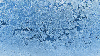 Abstract Christmas wallpaper. Ice crystals on frozen window glass pane. Frost drawing. Winter season pattern. Blue tinted background. Cold and crystal. Macro