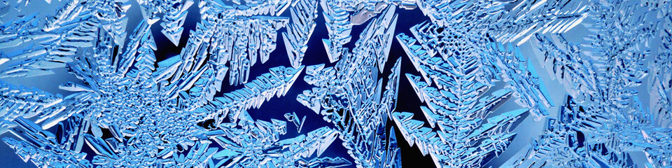 Christmas banner. Ice crystals on frozen window glass. Frost drawing. Pattern of leaves and stems of fantastic plant. Blue tinted header. Winter season theme. Cold and crystal. Macro