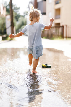Little girl walks barefoot through puddles raising a fan of spray. High quality photo