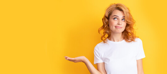 pondering redhead woman presenting product on yellow background with copy space. Beautiful woman...