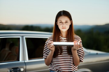 A woman holds a flashlight standing by her car on a nature trip to a campground and smiles. Travel as a lifestyle