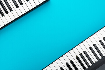 Top view of piano keyboards with copy space. Minimalist photo of midi keyboards over blue. Two piano style keyboards on turquoise background.