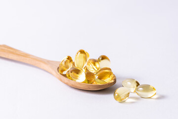 Omega 3 cod liver oil capsules in the wooden spoon on white background, macro view. Health care concept, copy space for your design.
