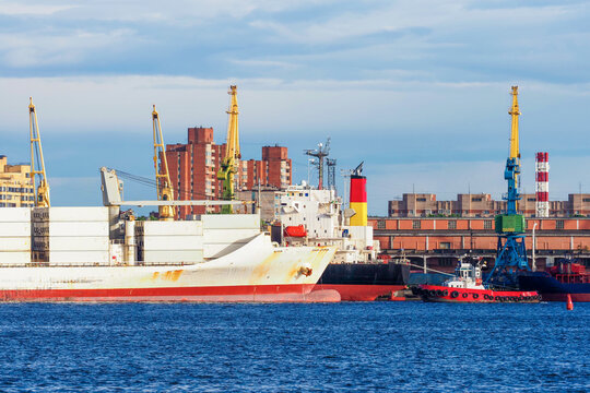Loaded barge and tug in the city cargo port. Port life against the backdrop of the city, St. Petersburg, Russia