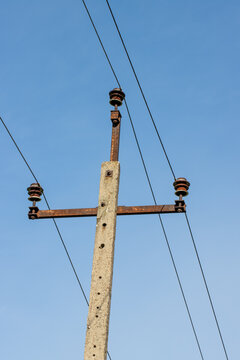 Vintage electricity pole with live wires and ceramic insulators against blue sky in Poland