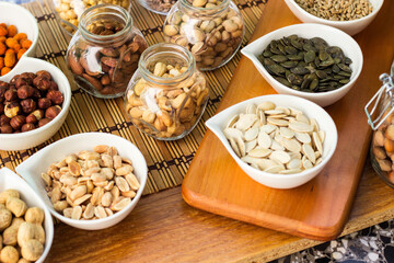 Rustic wood table filled with a large assortment of nuts like pistachios, hazelnut, pine nut, almonds, pumpkin seeds, sunflower seeds, peanuts, cashew and walnuts