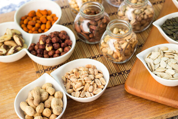 Rustic wood table filled with a large assortment of nuts like pistachios, hazelnut, pine nut, almonds, pumpkin seeds, sunflower seeds, peanuts, cashew and walnuts