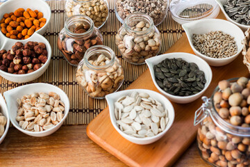 Rustic wood table filled with a large assortment of nuts like pistachios, hazelnut, pine nut, almonds, pumpkin seeds, sunflower seeds, peanuts, cashew and walnuts