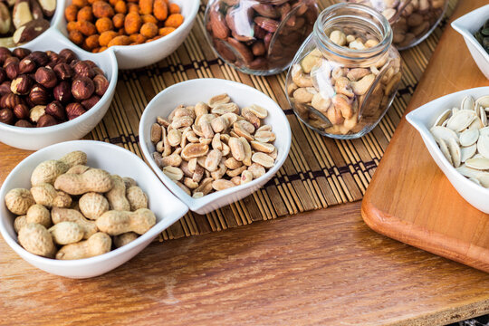 Rustic wood table filled with a large assortment of nuts like pistachios, hazelnut, pine nut, almonds, pumpkin seeds, sunflower seeds, peanuts, cashew and walnuts