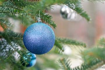 Blue textured christmas ball hanging on christmas tree with blurred background oudoors. Selective focus.