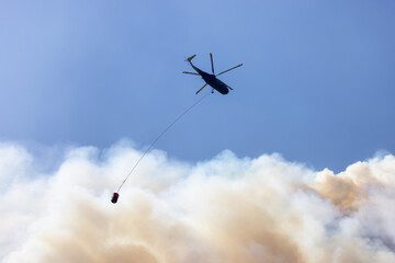 Wildfire Service Helicopter flying over BC Forest Fire and Smoke on the mountain near Hope during a hot sunny summer day. British Columbia, Canada. Natural Disaster