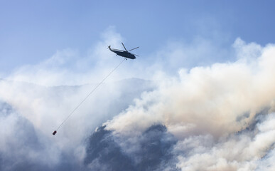 Wildfire Service Helicopter flying over BC Forest Fire and Smoke on the mountain near Hope during a hot sunny summer day. British Columbia, Canada. Natural Disaster