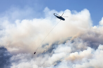 Wildfire Service Helicopter flying over BC Forest Fire and Smoke on the mountain near Hope during a hot sunny summer day. British Columbia, Canada. Natural Disaster