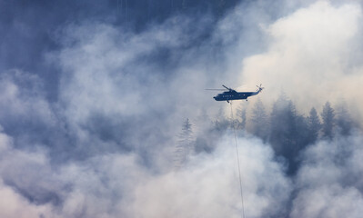 Wildfire Service Helicopter flying over BC Forest Fire and Smoke on the mountain near Hope during a hot sunny summer day. British Columbia, Canada. Natural Disaster