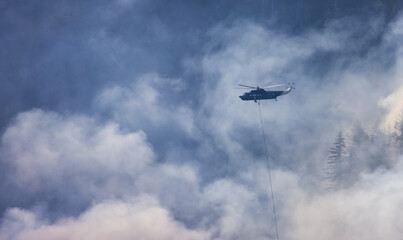 Wildfire Service Helicopter flying over BC Forest Fire and Smoke on the mountain near Hope during a hot sunny summer day. British Columbia, Canada. Natural Disaster