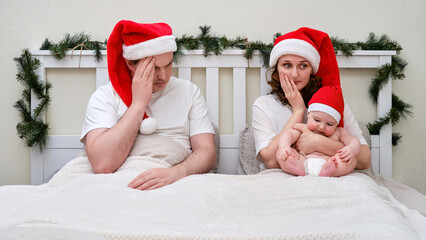 Sad husband and wife with baby on bed decorated for christmas and new year, family couple in home...
