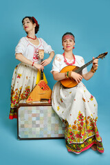 Women musicians in Russian folk dresses with musical instruments on a blue studio background. Happy...