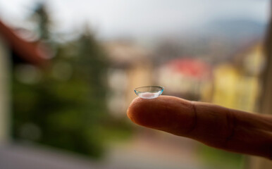Close of a contact Lens on an index finger against blurred background. Eyesight vision correction, Healthcare and Medicine concept