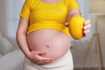 Yellow lemon in the hands of a pregnant woman, home living room