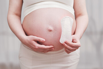 A pregnant woman holds a sanitary pad in her hands, home living room