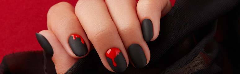 Close up womans hand with halloween manicure on red background holding fabric. Manicure, pedicure beauty salon concept - obrazy, fototapety, plakaty