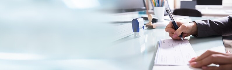 Businessman Filling The Cheque On Desk