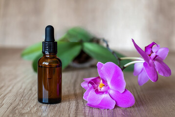 Glass brown bottle of serum with pipette on a wooden table with a blooming purple orchid, close up