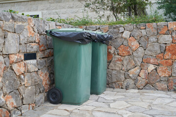 Green garbage cans next to the stone wall