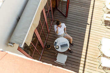 Top-down of young female copywriter typing text on laptop keyboard sitting on wooden terrace. Top view of woman in casual look working remotely from home