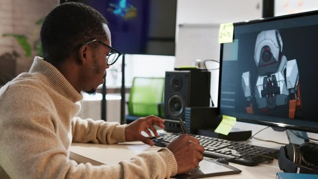 African American male artist designer draws on a tablet a 3D model of a dog robot for a computer game in the office of a project development studio.