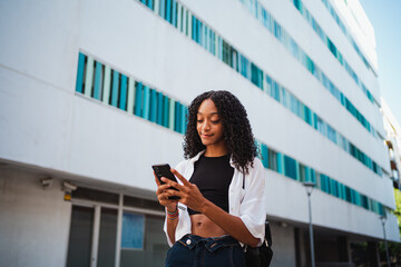 Fototapeta premium African woman texting to her family and friends on her cellphone while she is walking in the city.