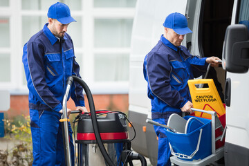 Two Male Janitor Unloading Cleaning Equipment From Vehicle