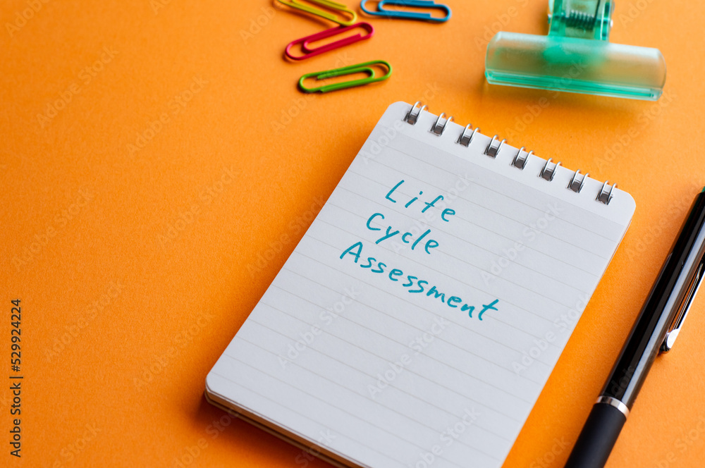 Poster there is a notebook with the word life cycle assessment. it's placed on a color background.
