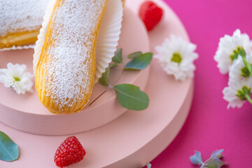  Eclairs cakes. Custard cakes with in powdered sugar on a pink podium on a Fuchsie...