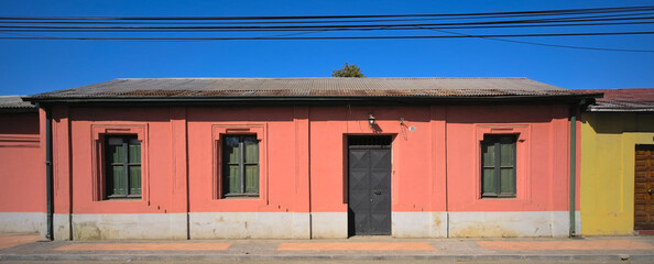 Facade of a one-floor traditional adobe house in a small south american town under blue sky (Talca,...