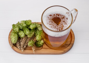 Mug with beer, fresh hops and ears of wheat on white wooden table, closeup