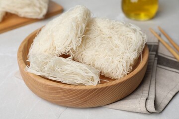 Wooden bowl with uncooked rice noodles on light table, closeup