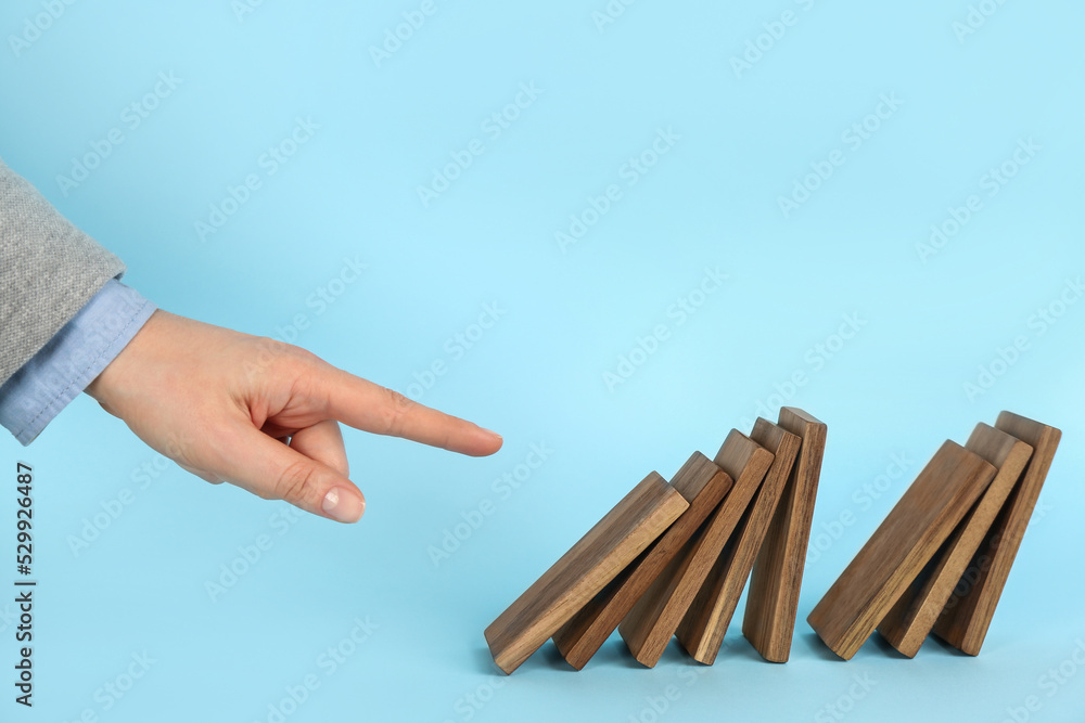 Wall mural Woman causing chain reaction by pushing domino tile on light blue background, closeup