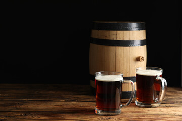 Glass mugs of delicious kvass and barrel on wooden table. Space for text