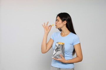 Fototapeta premium Beautiful woman eating potato chips on grey background. Space for text