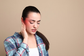 Woman suffering from ear pain on beige background, space for text