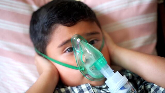 Sick child inhaling with nebulizer to reduce cough, lying at home, taking medication while breathing through face mask. Bronchitis and asthma treatments for children.