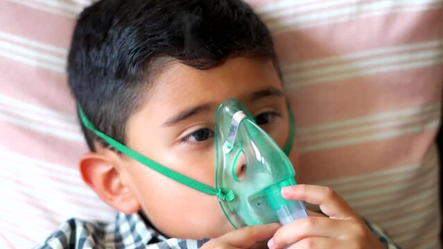 Sick child inhaling with nebulizer to reduce cough, lying at home, taking medication while breathing through face mask. Bronchitis and asthma treatments for children.