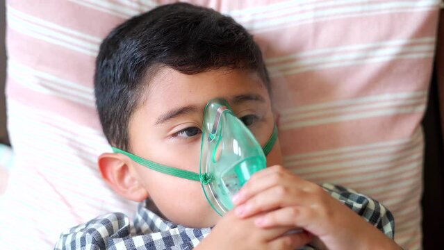 Sick child inhaling with nebulizer to reduce cough, lying at home, taking medication while breathing through face mask. Bronchitis and asthma treatments for children.