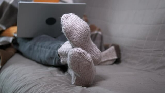 Relax in warm socks with computer. A calm child lay on the sofa in knitted clothes with her notebook. A concept of cozy time during winter period.