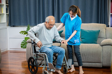Asian nurse assisting helping senior man patient get up from wheelchair for practice walking at...
