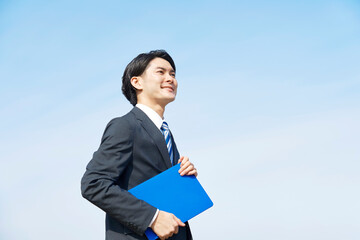 ノートパソコンを外で持つビジネスマン　青空背景