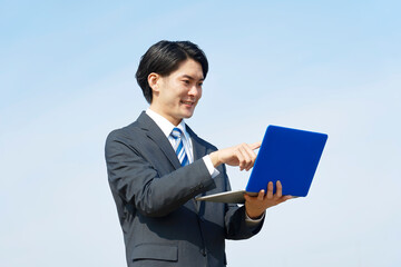 ノートパソコンを外で使うビジネスマン　青空背景