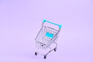 Empty shopping cart with light blue details floating on a pastel lilac background. Minimalist design with copy space. Concepts: market deals, seasonal sales and discounts, black friday.